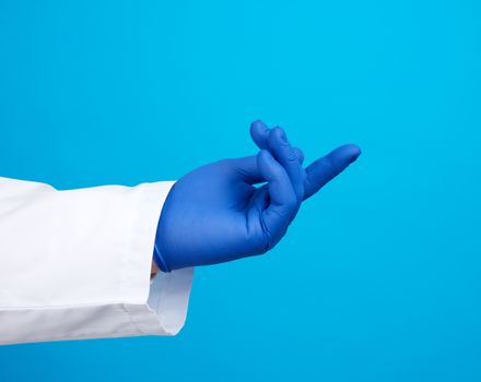 doctor’s hand is wearing a blue sterile rubber glove holding an object, blue background, element for a designer