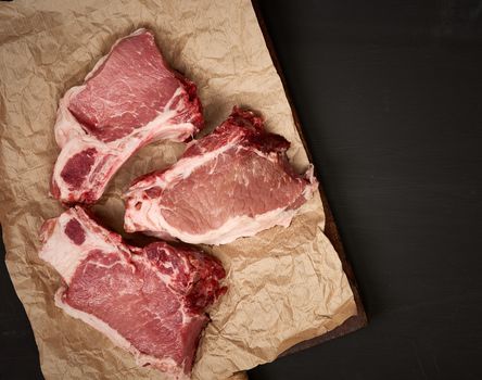 raw juicy pork slices of meat on the rib, food lies on brown parchment paper, black wooden background, top view