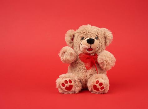 cute little brown teddy bear, toy is sitting on a red background, close up, copy space