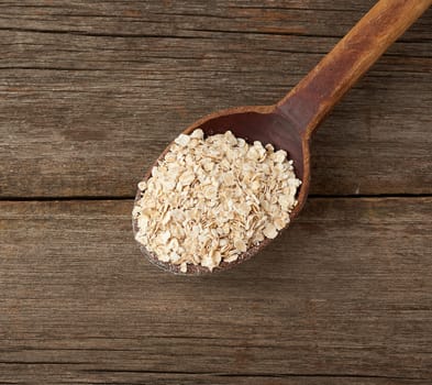 oatmeal flakes in a wooden spoon on the table, top view