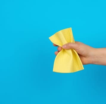 female hand holds a yellow rag sponge for cleaning, blue background