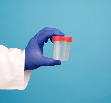 doctor in a white coat holds a empty plastic container for urine specimen, wearing blue sterile medical gloves