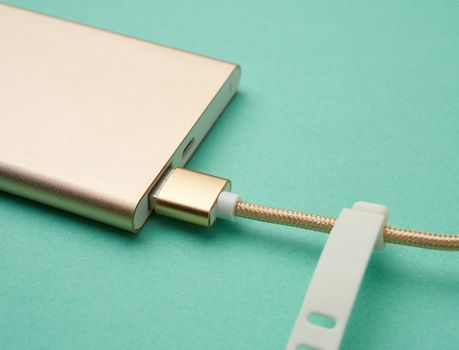 golden power bank and cord with a usb connector for recharging mobile devices on a green background, top view