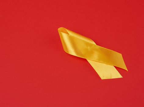yellow silk ribbon loop on a red background. Sarcoma bone cancer awareness, copy space