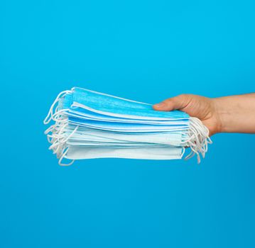 hand holds a stack of medical face masks against viruses and bacteria on a blue background, protective medical tool