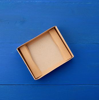 open empty brown cardboard box for transportation and packaging of goods on blue wooden background, top view.