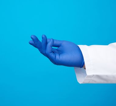 doctor’s hand is wearing a blue sterile rubber glove holding an object, blue background, element for a designer