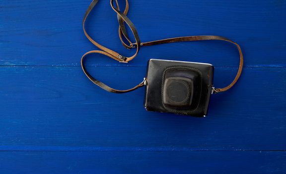 Vintage film camera in a leather case on a wooden blue background, top view