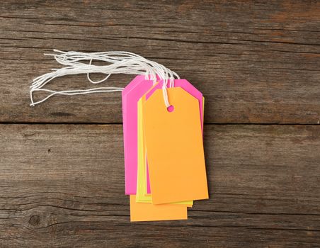 Stack empty color paper tags tied with white string. Price tag, gift tag, sale tag on a gray wooden background, close up