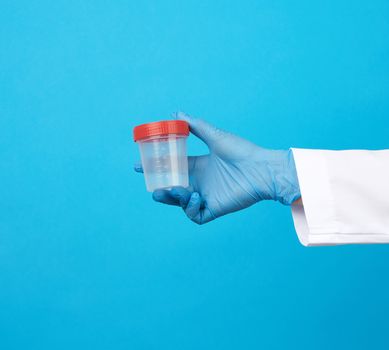 doctor in a white coat holds a empty plastic container for urine specimen, wearing blue sterile medical gloves