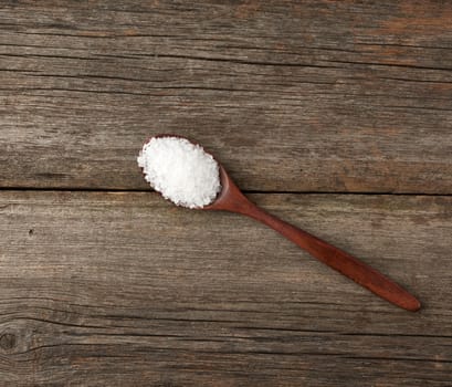 white coarse salt in a wooden spoon, gray table from old boards, top view