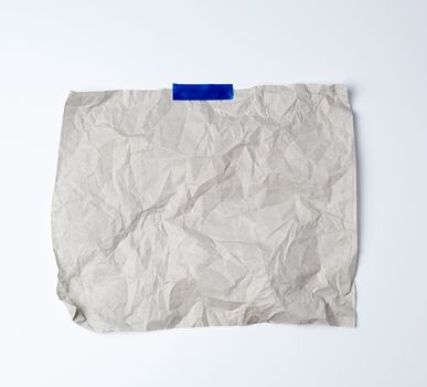 gray crumpled sheet of paper glued with blue adhesive tape on a white background, place for text