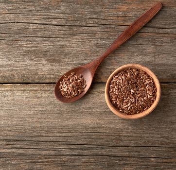 dry brown flax seeds in a brown wooden spoon on a gray wooden table from old boards, top view