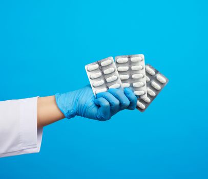 female hand with blue sterile gloves holds a pills in a blister, concept for drug treatment of diseases, blue background