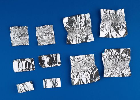 various crumpled foil used candy wrappers on a blue background, top view