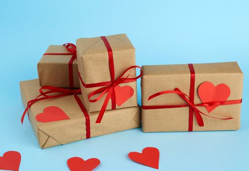 stack of wrapped gifts in brown kraft paper and tied with a red ribbon on a blue background, surprise and a gift for Valentine's Day February 14