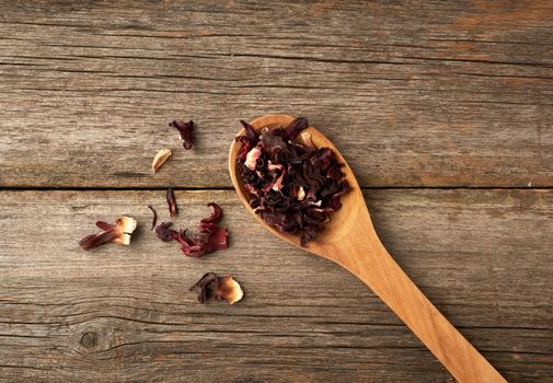 dry petals of red hibiscus in a wooden spoon, tea preparation, top view