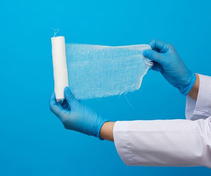 medic woman in white coat holds a twisted gauze bandage, blue background, medical item for bandaging human limbs