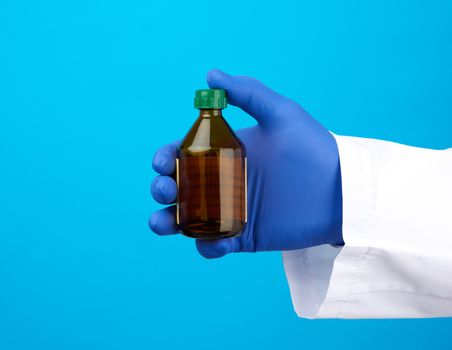 hand in blue latex medical glove holds a brown glass bottle for medicines, blue background