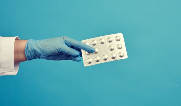 female hand with blue sterile gloves holds a pills in a blister, concept for drug treatment of diseases, blue background