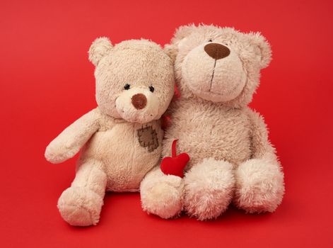 two teddy beige bears sitting huddled together, toys on red background, friendship and love concept