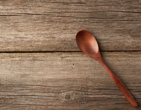 empty brown wooden spoon on a gray wooden surface from old boards, top view