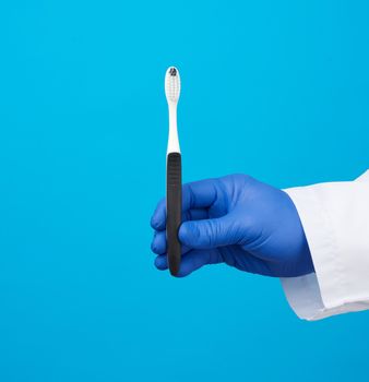 doctor therapist is dressed in a white robe uniform and blue sterile gloves holding a toothbrush, daily brushing concept, blue background