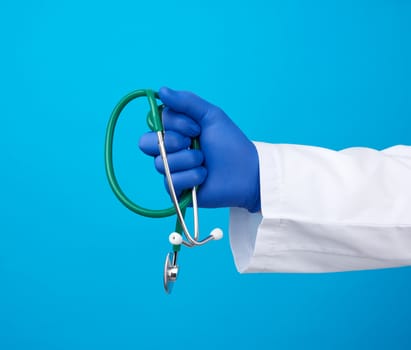 male doctor in a white medical coat stands and holds a green stethoscope on a blue background, copy space