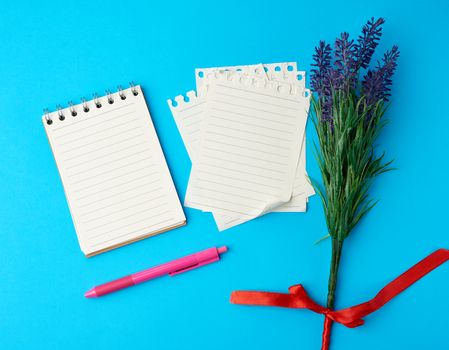 open notebook with white sheets and a pink plastic pen on a blue background, near a bouquet of flowers, close up