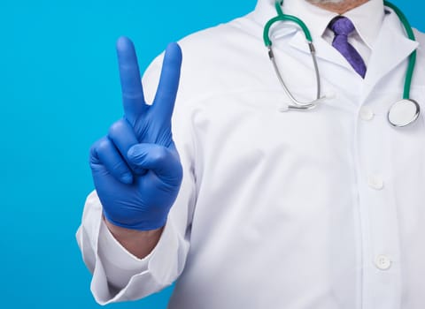male hand in blue sterile medical gloves shows victory gesture, concept of victory over the disease, positive emotions