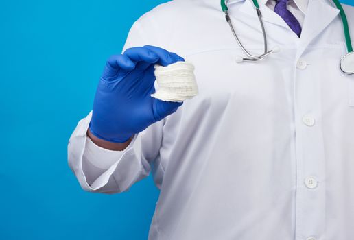 male doctor in a white coat, blue latex medical gloves holding a stack of cotton cosmetic discs, blue background
