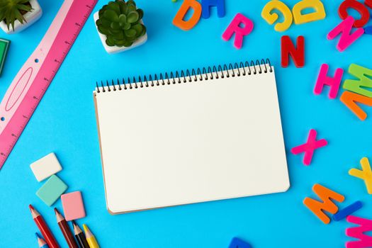 set of different school colorful items for learning at school on a blue background, open notebook in the middle with blank white sheets, top view, concept of back to school