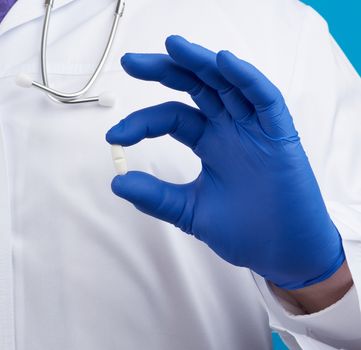 male hand in blue sterile gloves holds an oval white pill, medical treatment concept for diseases,  close up