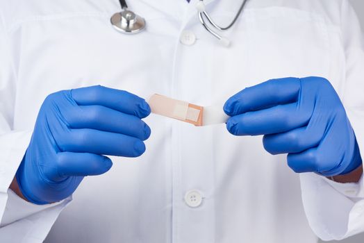 male doctor in a white coat, blue latex medical gloves holds a textile medical adhesive plaster, close up