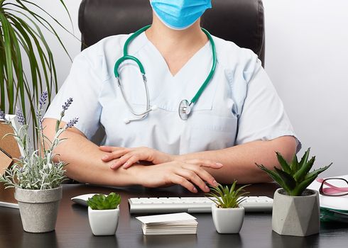 doctor gloves sits at a white work table in his office, concept of patient reception in the clinic, hands joined in front of the chest, focused pose