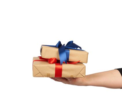 hand holds a stack of wrapped gifts in brown craft paper with tied silk bows, subject is isolated on a white background