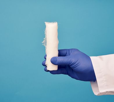male hand in blue sterile gloves holds a white twisted gauze medical bandage on a blue background, treatment of injuries