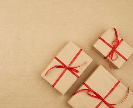 gift wrapped in brown kraft paper and tied with a thin silk ribbon on a background of paper, top view. Congratulations on Valentine's Day February 14