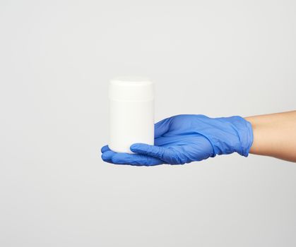 hand in blue sterile glove holds white plastic jar with pills on white background, close up