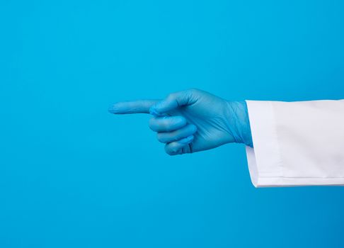 medic woman in white coat, wearing in blue sterile gloves, showing hand gesture indicating the subject, blue background