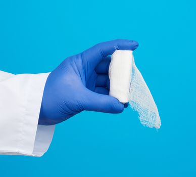 male hand in blue sterile gloves holds a white twisted gauze medical bandage on a blue background, treatment of injuries