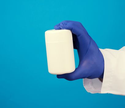 male doctor in a white medical coat and blue latex gloves holds a white plastic jar of pills, close up