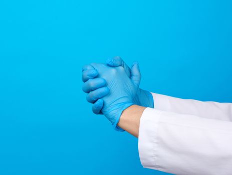 two hands in blue latex medical gloves joined in a handshake on a blue background, support concept