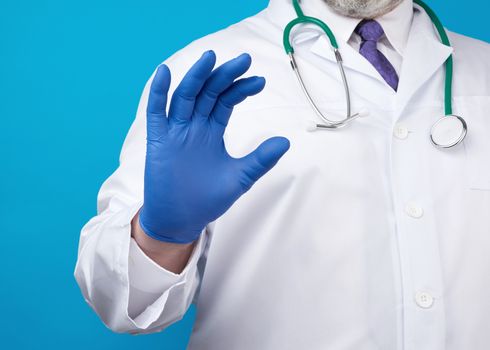 doctor’s hand is wearing a blue sterile rubber glove holding an object, blue background, close up
