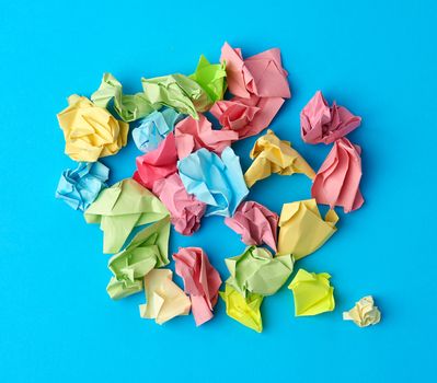 crumpled multi-colored paper stickers, top view, blue background, close up