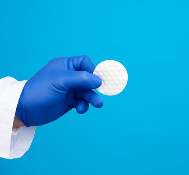 hand hold white cotton round disc for cosmetic procedures on a blue background, close up