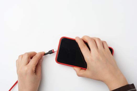 two female hands are holding a smartphone with a blank black screen and cable, charging process, white background, top view