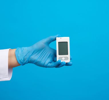 hand in blue sterile gloves holds a white blood glucose meter for measuring blood sugar, blue background