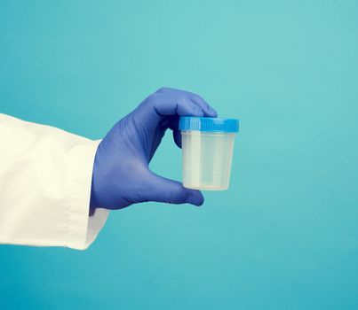 male doctor in a white coat holds a empty plastic container for urine specimen, wearing blue sterile medical gloves