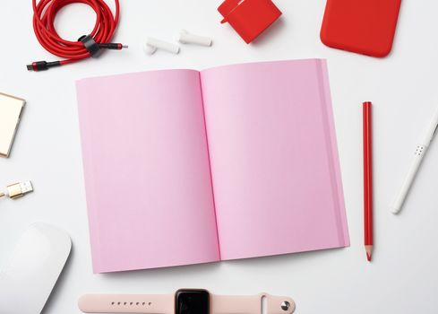pink paper notebook, power bank with cable, red smartphone, headphones, wireless mouse, smart watch on white background, workplace, top view